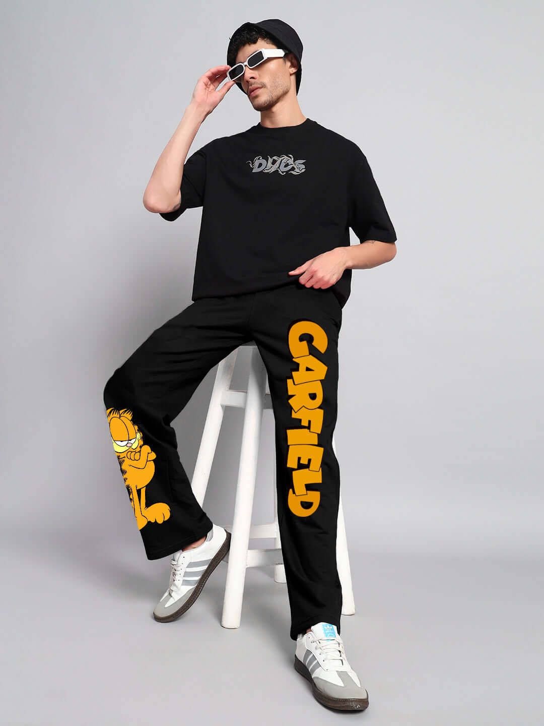 Model wearing black SMUG GARFIELD relaxed fit jogger, featuring Garfield graphic and logo, seated against a gray backdrop.