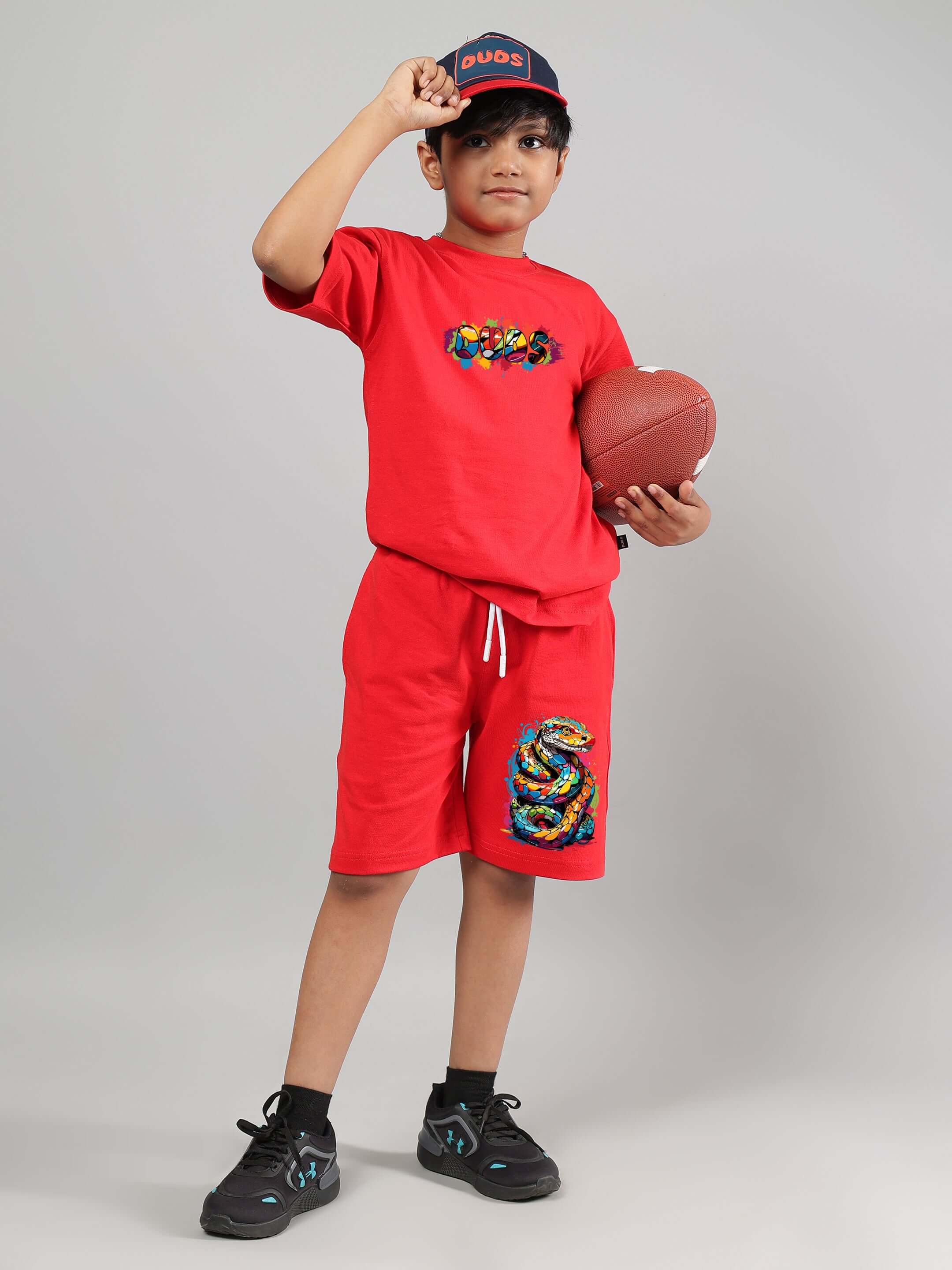 Boy wearing a red snake skin outfit holding a football, showcasing children's sportswear from DUDS.