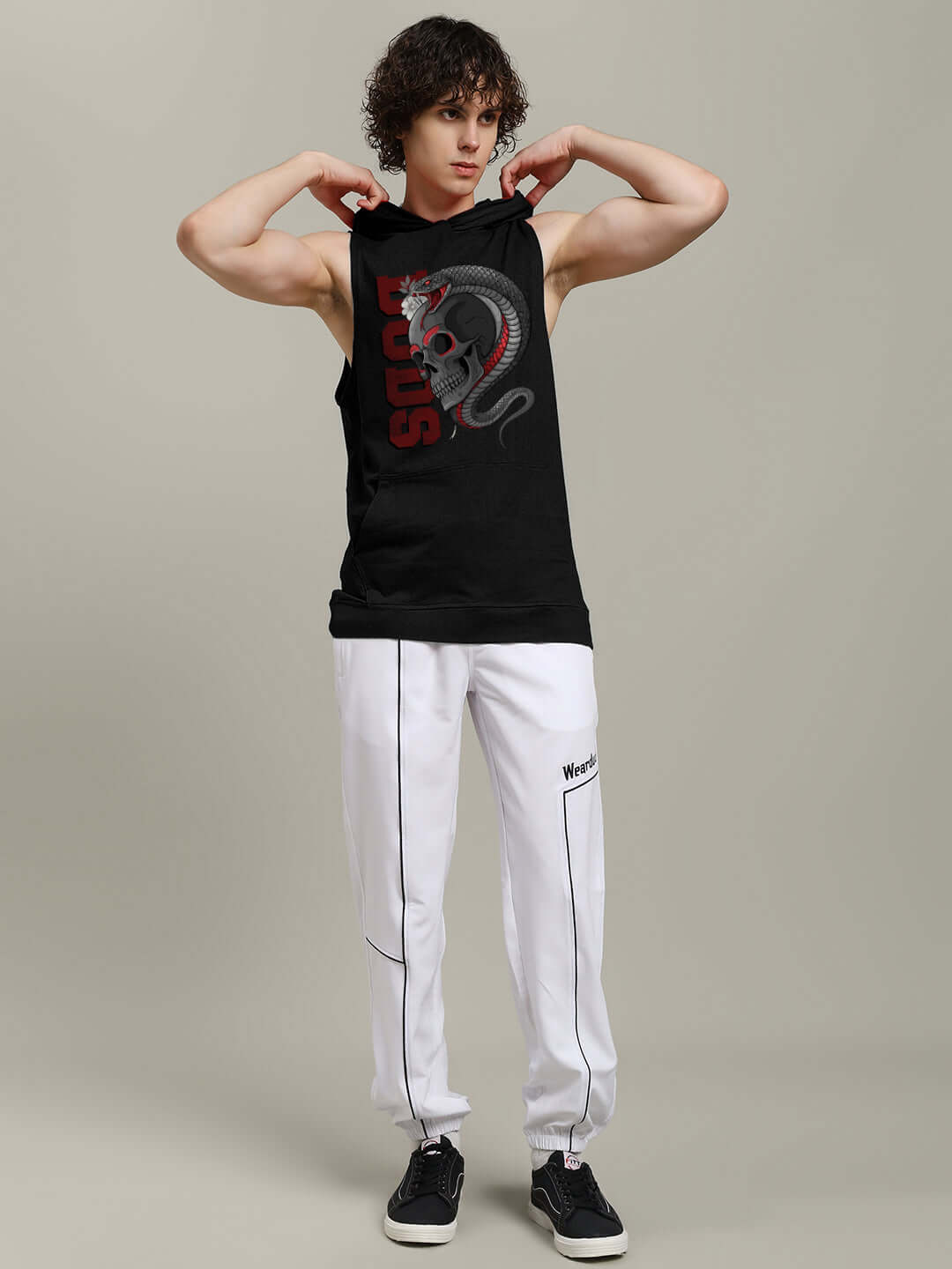 Man wearing a black hooded t-shirt with a snake and skull design, paired with white joggers, in a gym-ready stance.