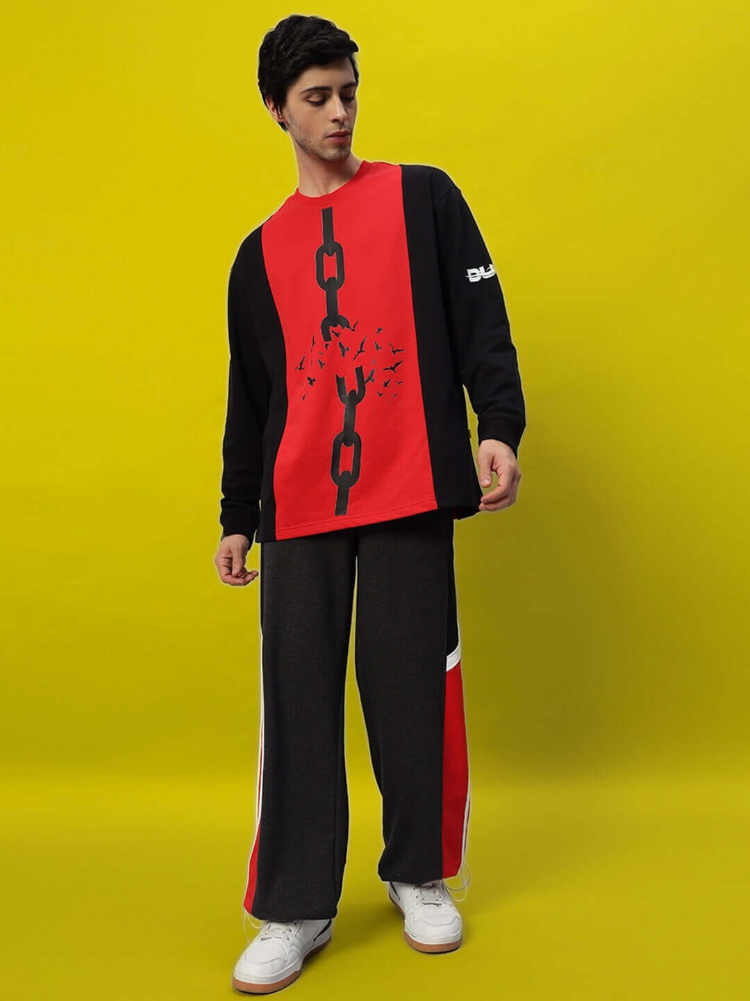 Model wearing Snicker Relaxed-Fit Joggers in dark grey and red, styled with a matching top against a yellow background.