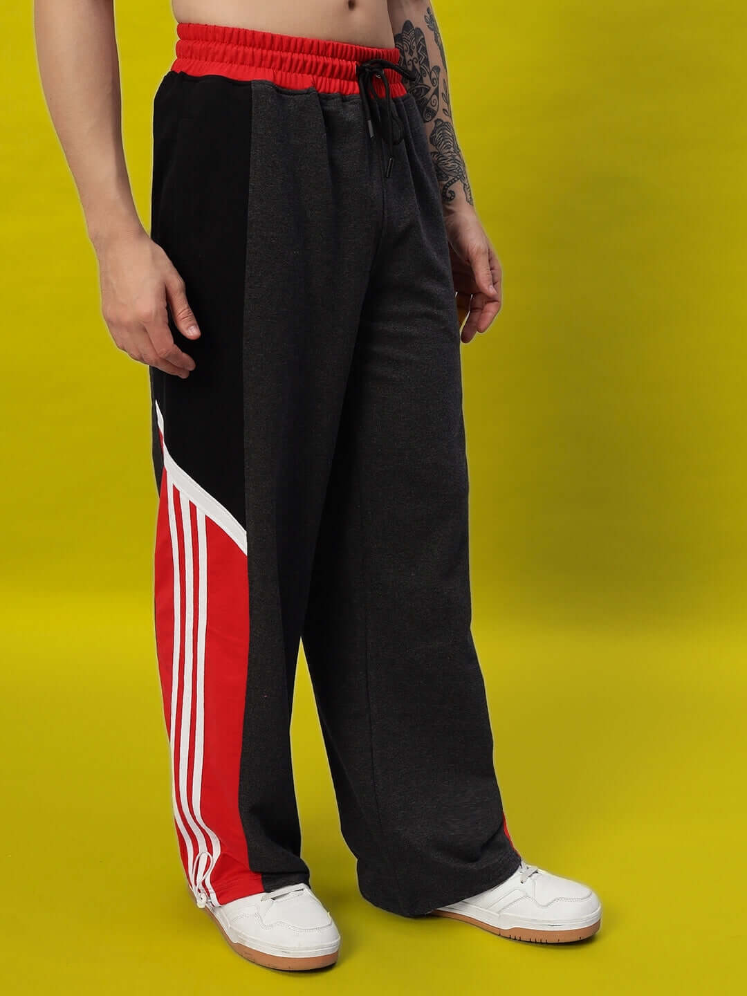 Model wearing Snicker Relaxed-Fit Joggers in dark grey with red accents showcasing casual style on yellow background.