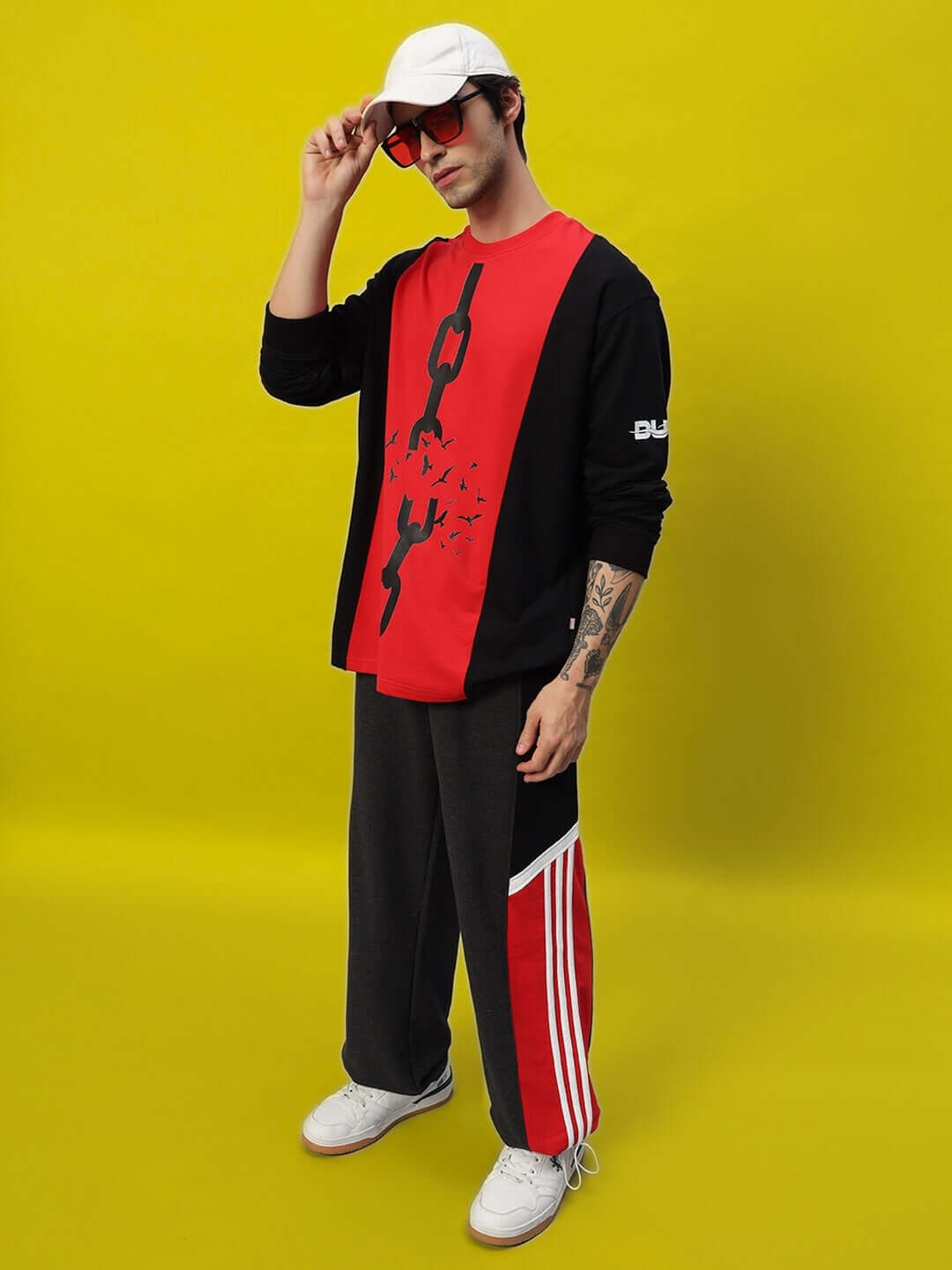 Model wearing Snicker Relaxed-Fit Joggers in Dark Grey-Red, showcased with casual red top and cap against yellow background.