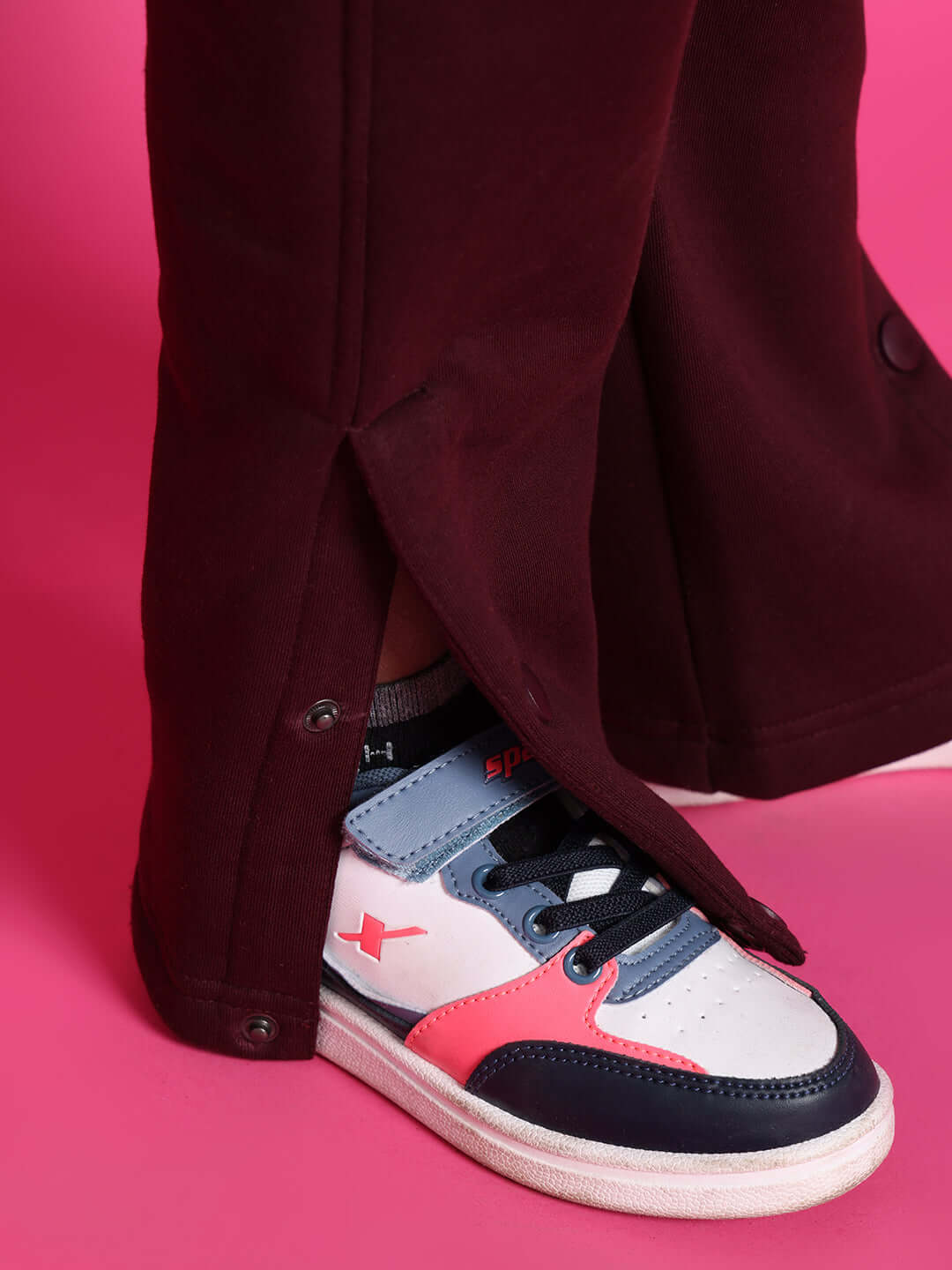 Close-up of wine-colored Snoopy fleece pant for boys and girls, featuring side snaps and worn with colorful sneakers, on a pink background.