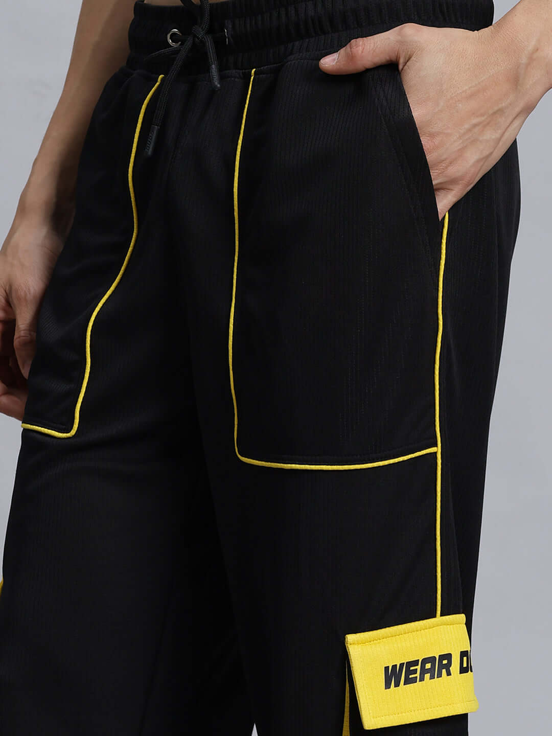 SOCCER REGULAR FIT CARGO JOGGER BLACK Close-up of black soccer cargo joggers with yellow piping, featuring side pockets and a prominent 'Wear Duds' patch.