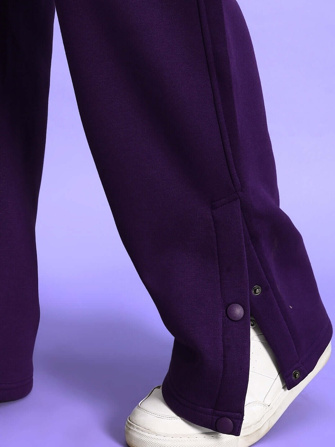 SOOTY COTTON FLEECE PANT PURPLE with adjustable button details and white sneakers on a purple background.
