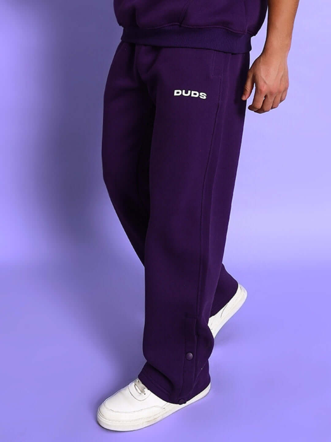 Person wearing SOOTY COTTON FLEECE PANT PURPLE with sneakers on purple background showcasing streetwear style.