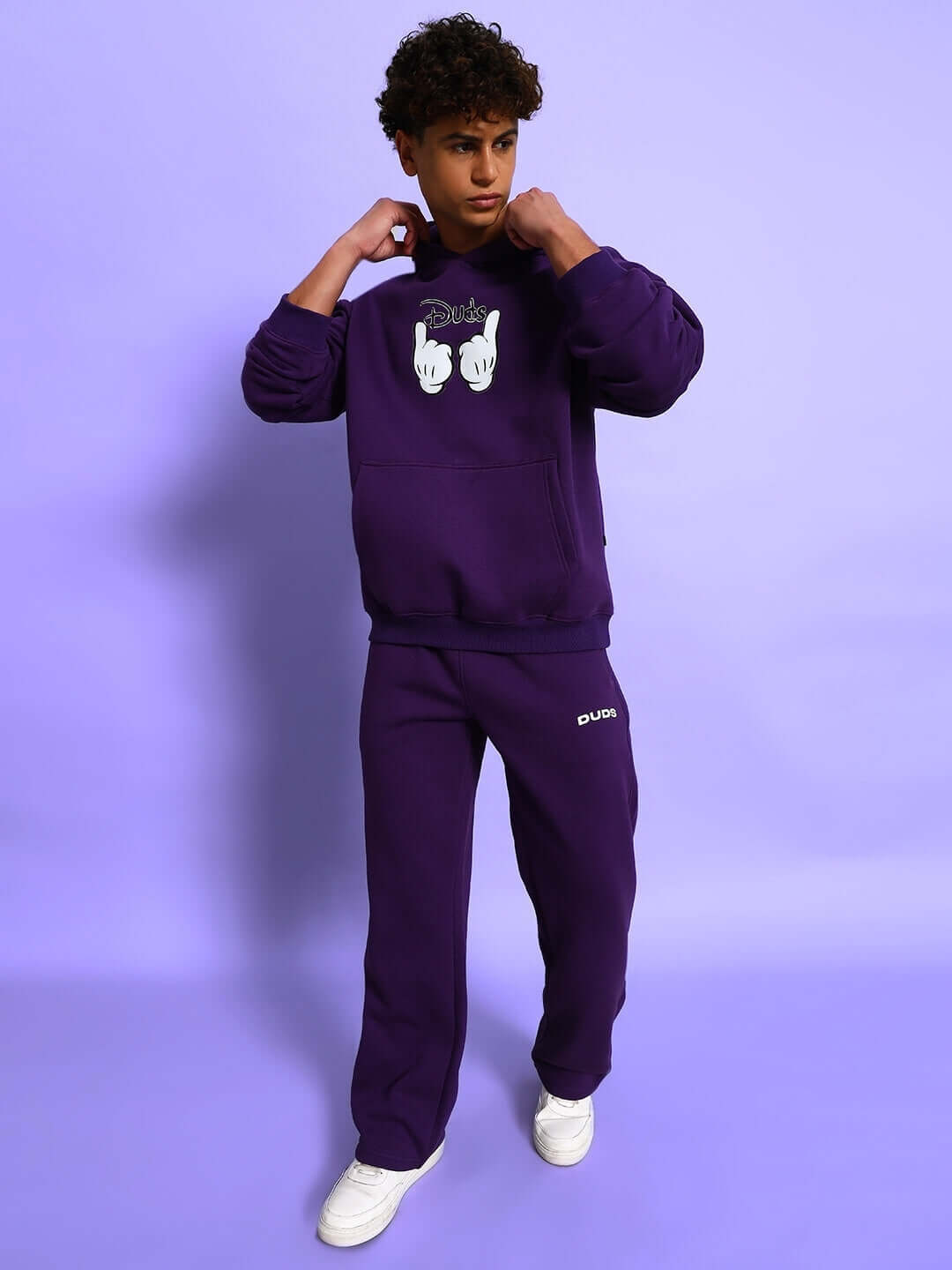 Young man wearing SOOTY COTTON FLEECE PANT PURPLE paired with matching sweatshirt, showcasing streetwear style on a purple background.