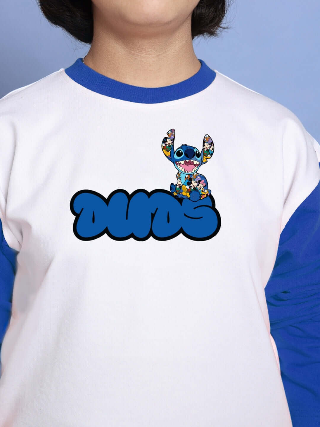 Child wearing a white-blue top featuring a cartoon design and the word 'DUOS' graphic with a playful character, close-up view.