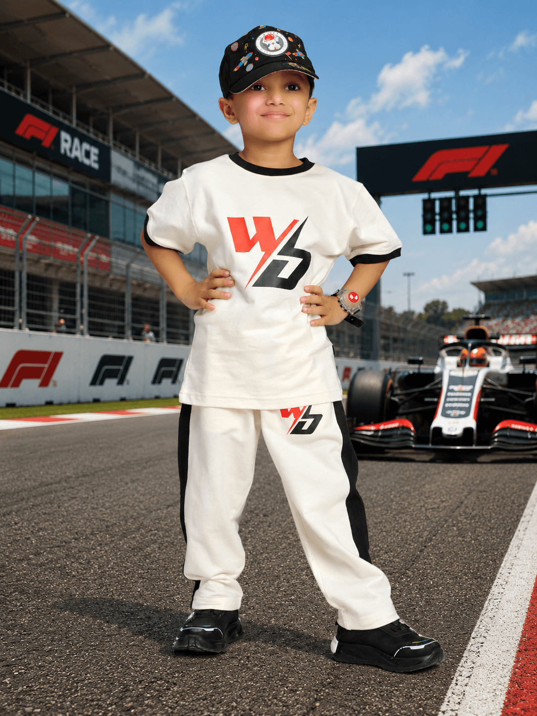 SPEED SURGE JOGGER FOR BOYS AND GIRLS WHITE BLACK worn by a child at a race track with a racing car in the background.