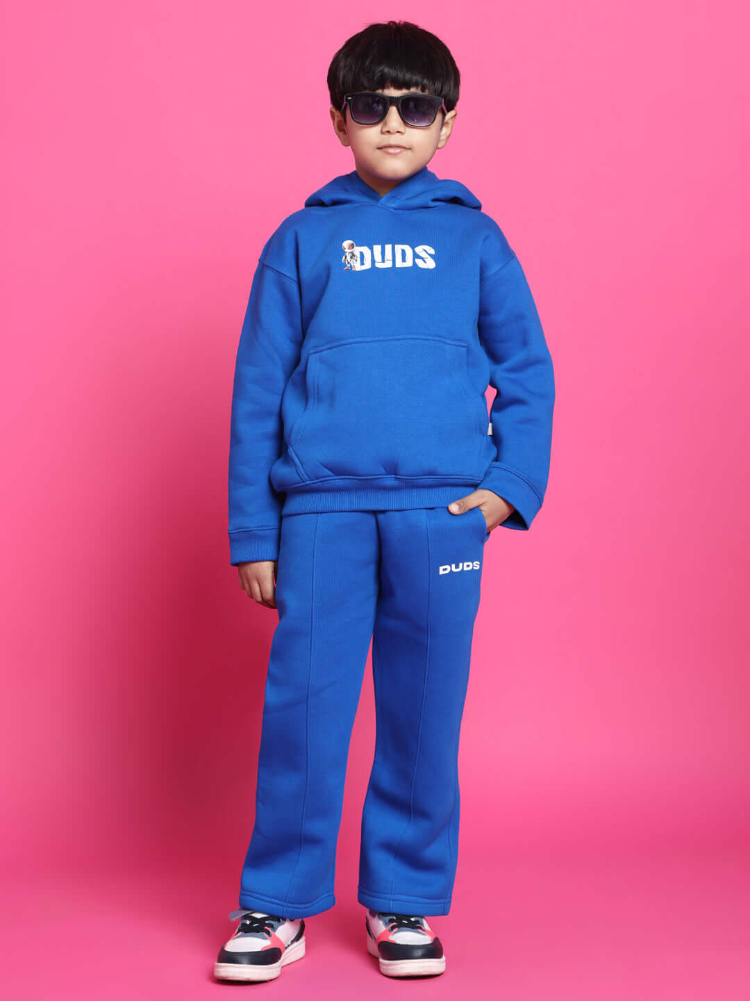 Child wearing blue SPIDERROBO fleece pants and hoodie in front of pink background.
