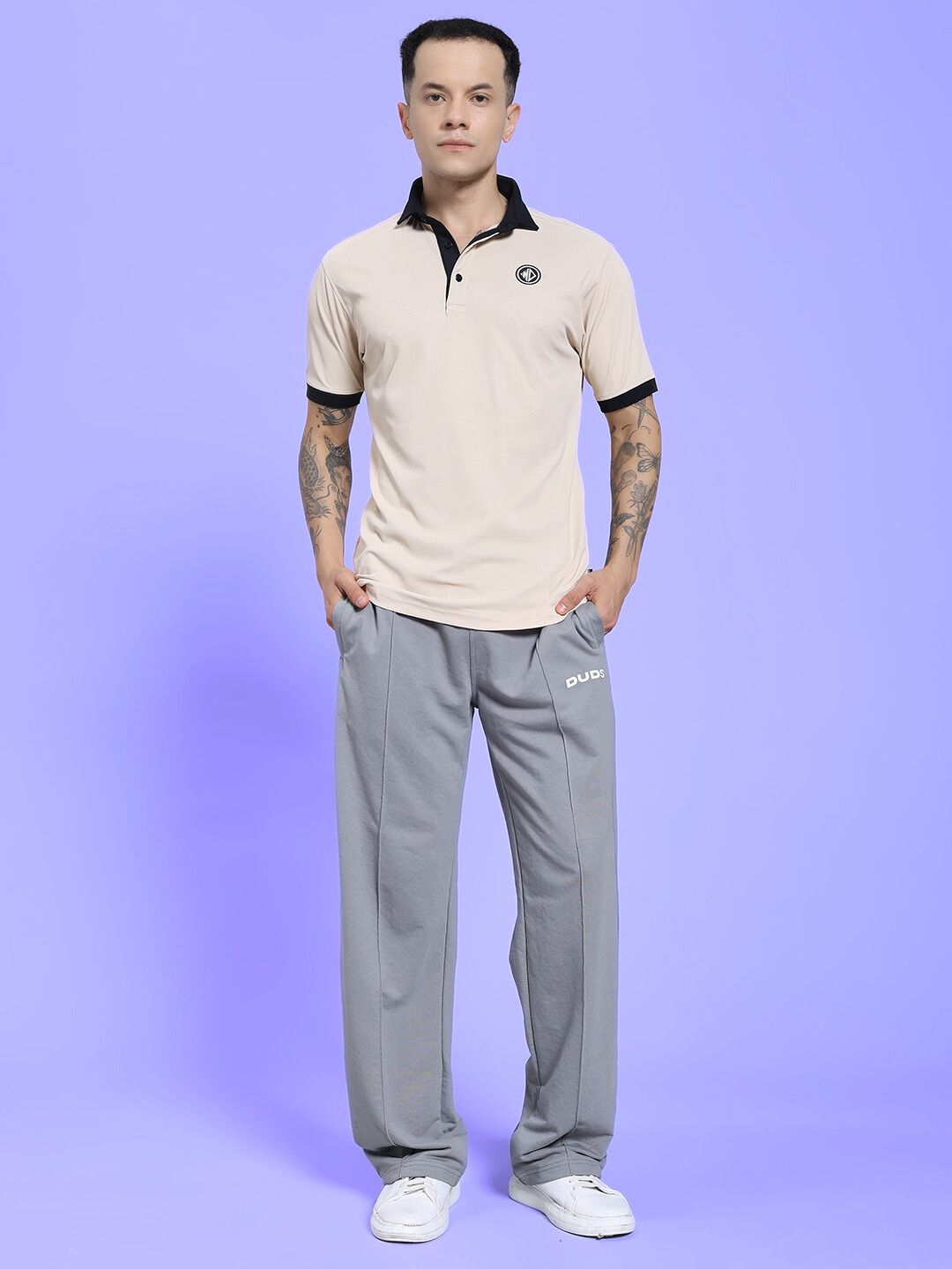 Man wearing SPIRAL RELAXED-FIT JOGGERS GREY and beige polo shirt against a purple background.