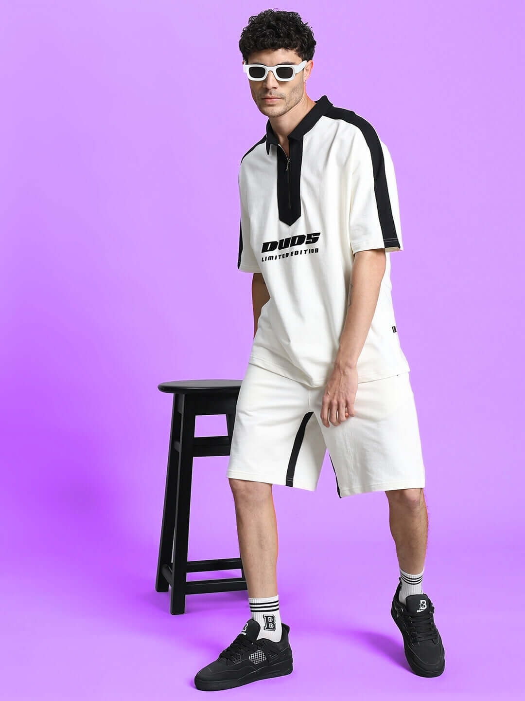 Man wearing SPLINTER REGULAR FIT SHORTS OFF WHITE with matching shirt, standing against a purple background in stylish pose.