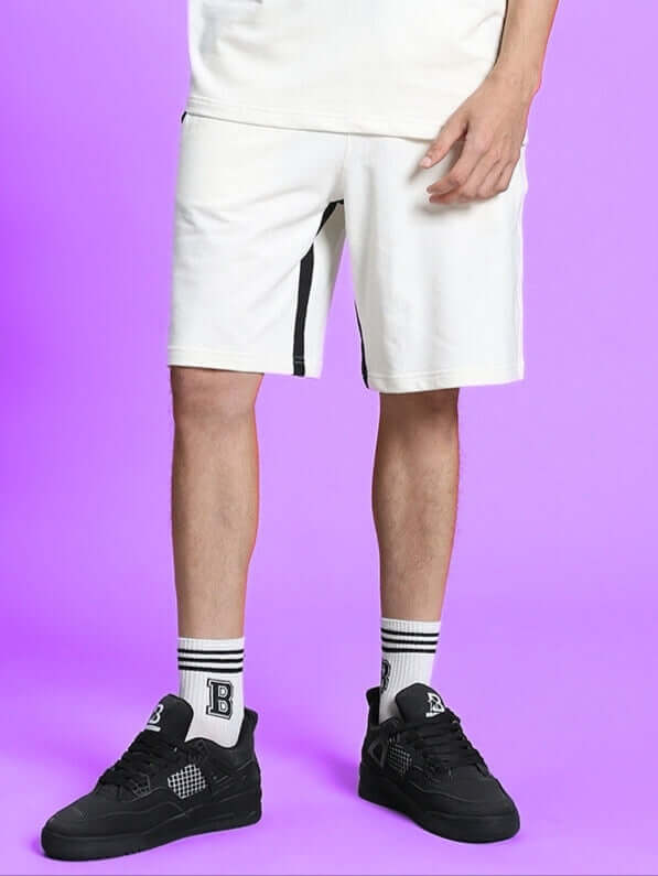 Model wearing SPLINTER REGULAR FIT SHORTS OFF WHITE against purple background