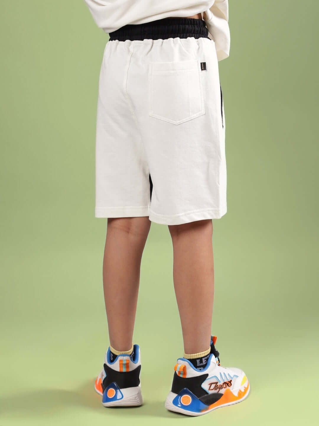 Child wearing Splinter Shorts for Boys & Girls Off-White, back view, showing comfortable and stylish design, paired with sneakers.