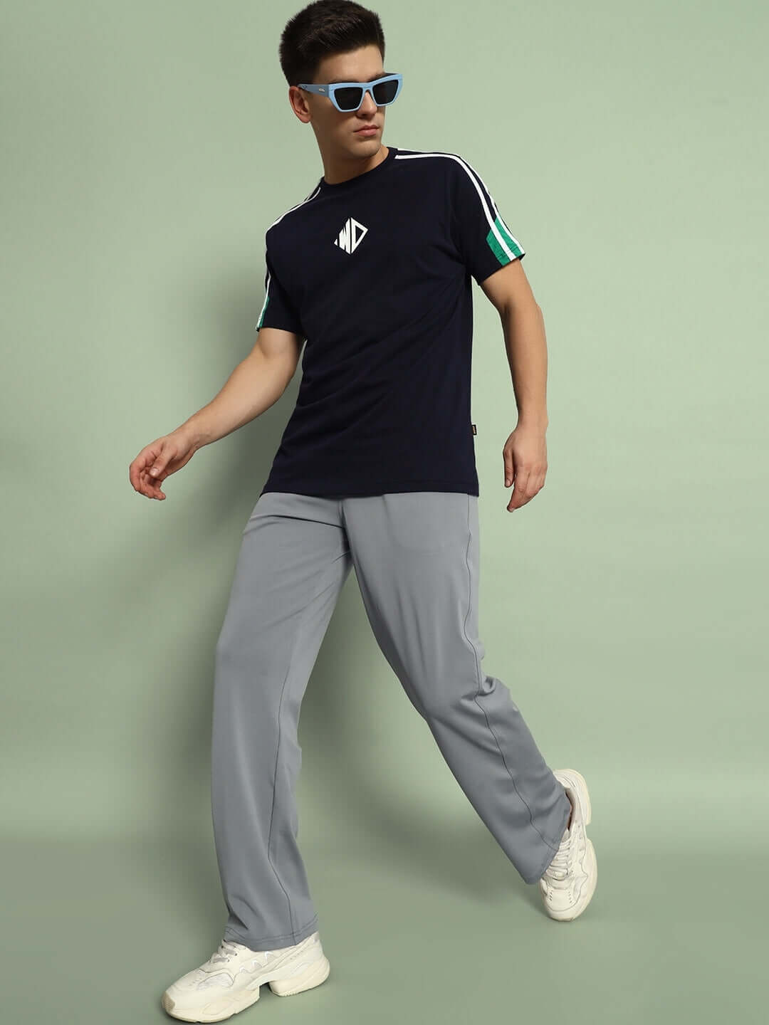 Model wearing grey Springy Relaxed Fit Joggers paired with a navy t-shirt and white sneakers on a light green background.