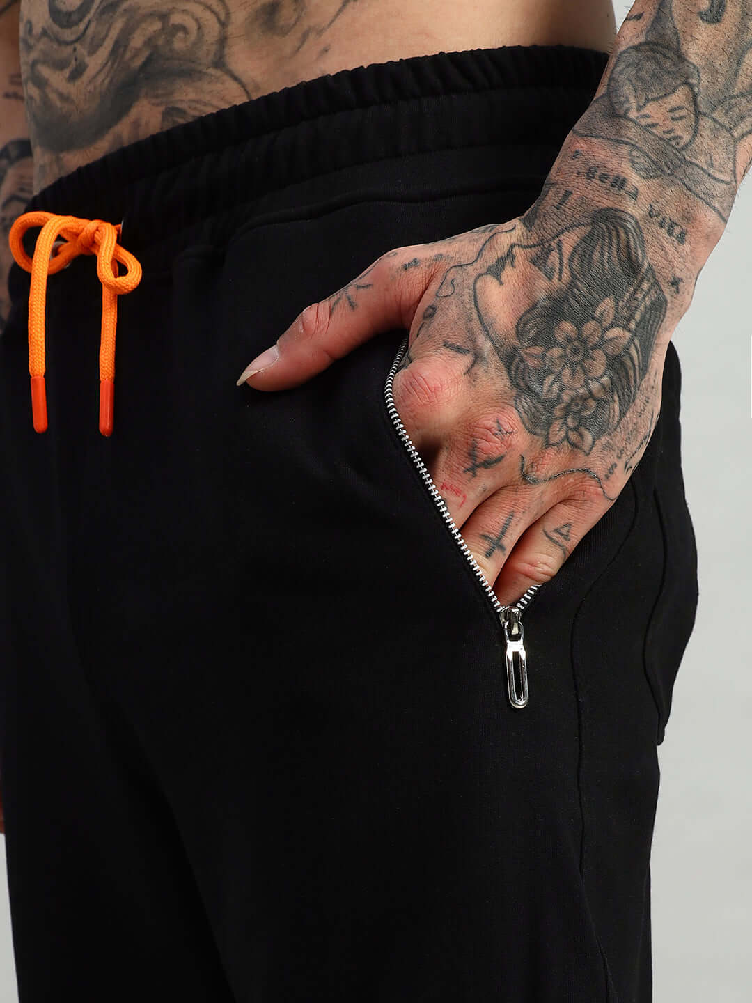 Person wearing black Squall Joggers by DUDS with orange drawstrings and zippered pocket.