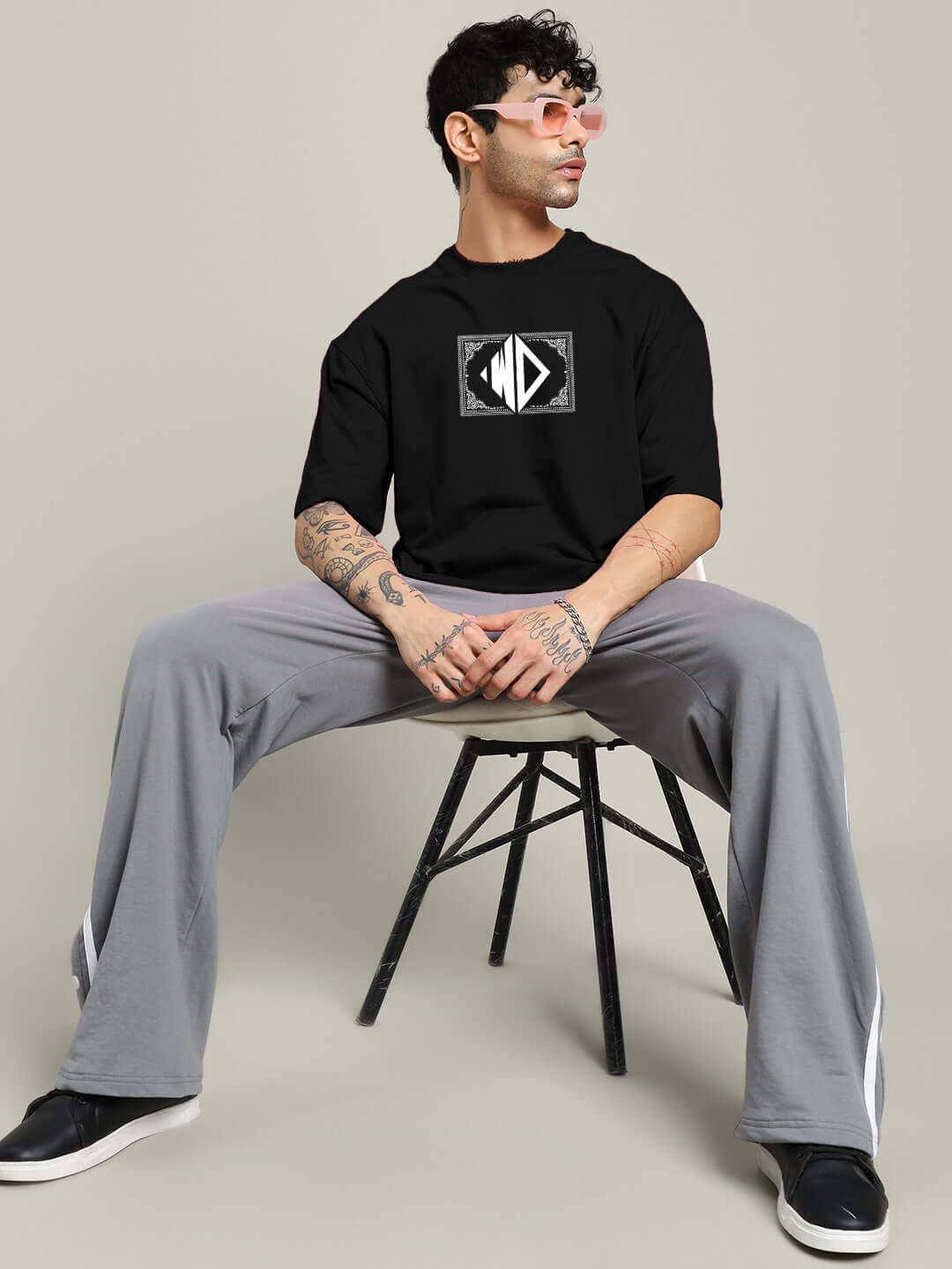 Man wearing black square frame oversized t-shirt made of premium cotton, sitting on a chair with a neutral background.