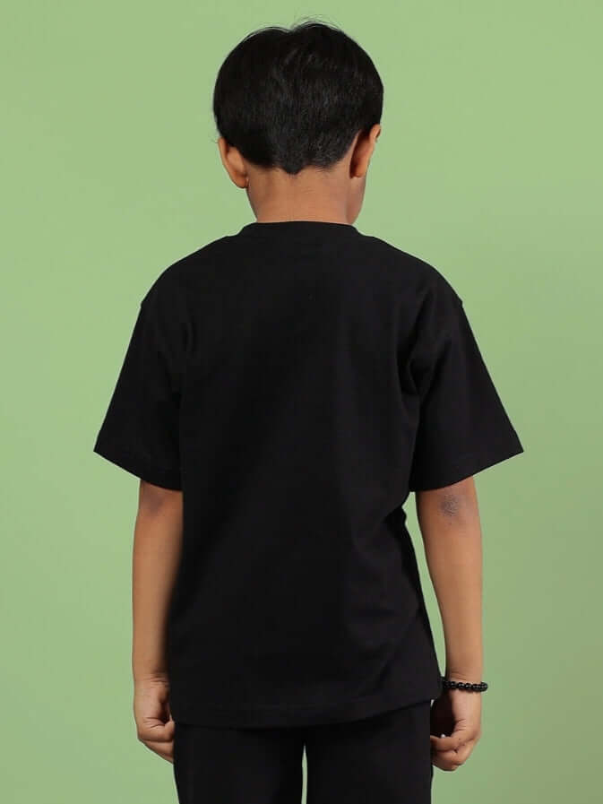 Child wearing black Squid Game t-shirt, back view, on a green background.
