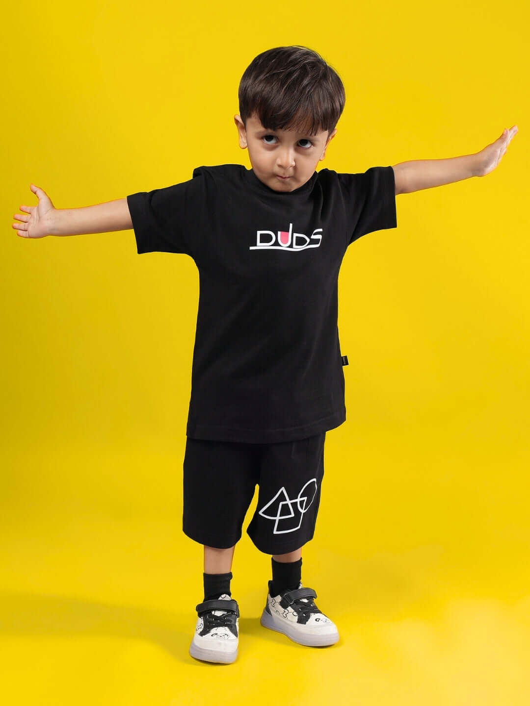 Child wearing SQUID BATTLE CO-ORD FOR BOYS & GIRLS BLACK outfit by DUDS, standing with arms outstretched in front of yellow background.