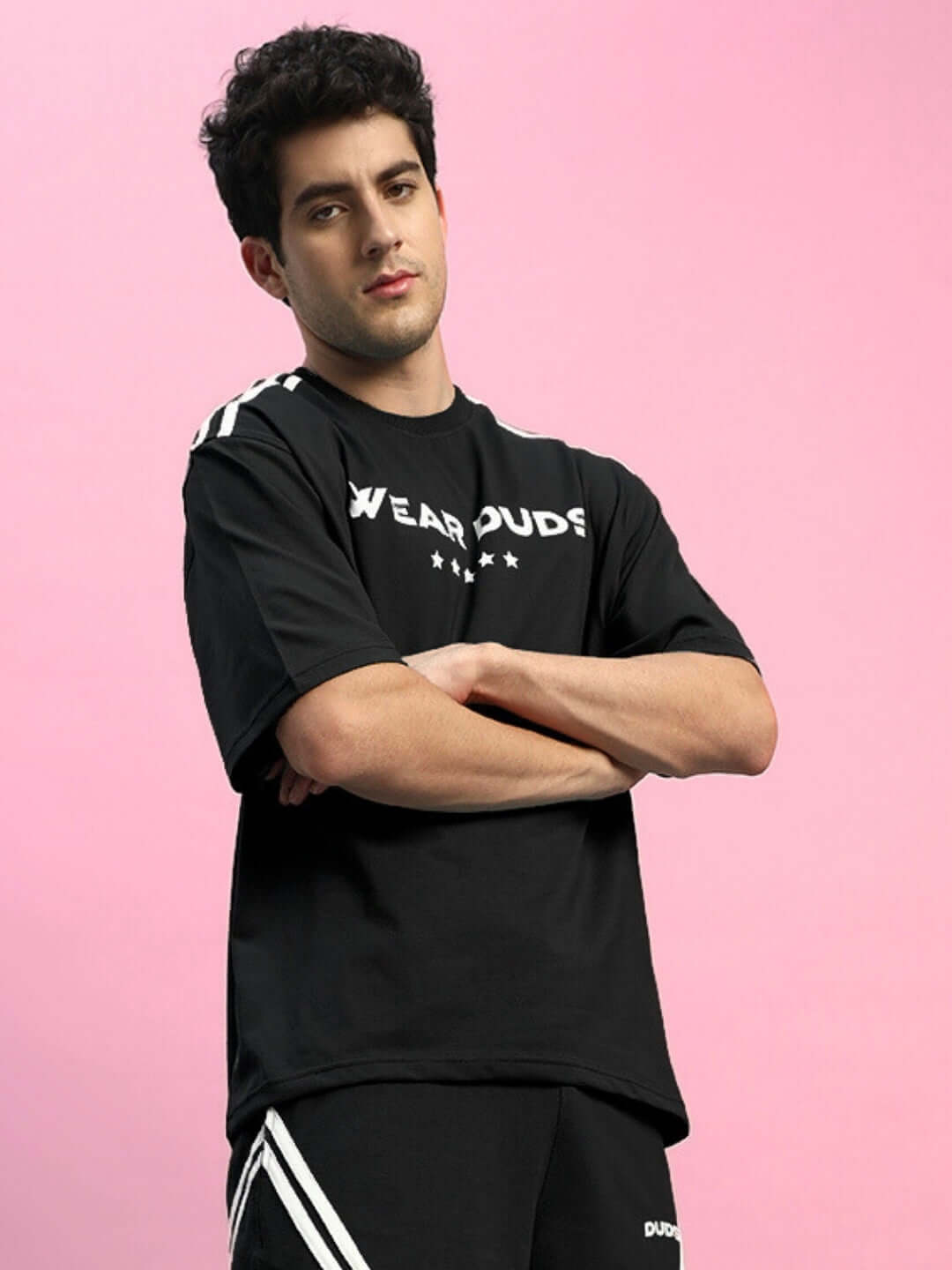 Model wearing STAR JUMPER OVER-SIZED T-SHIRT BLACK against a pink background, showcasing the casual and trendy fit.