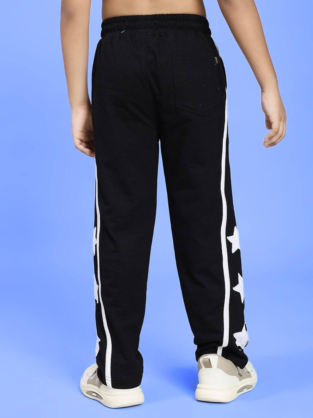 Child wearing STELLAR RELAXEDFIT JOGGER FOR BOYS AND GIRLS BLACK with white star patterns on a blue background.