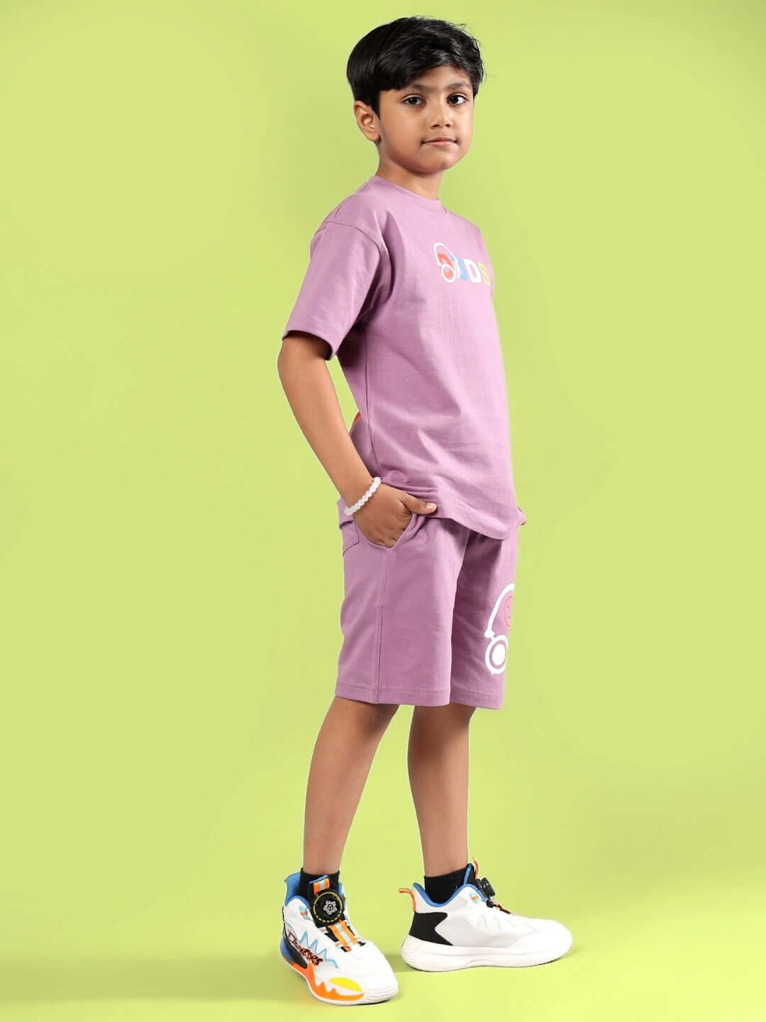 Child wearing STOIC CO-ORD FOR BOYS & GIRLS PULM PURPLE, showcasing stylish matching top and shorts set against a green background.