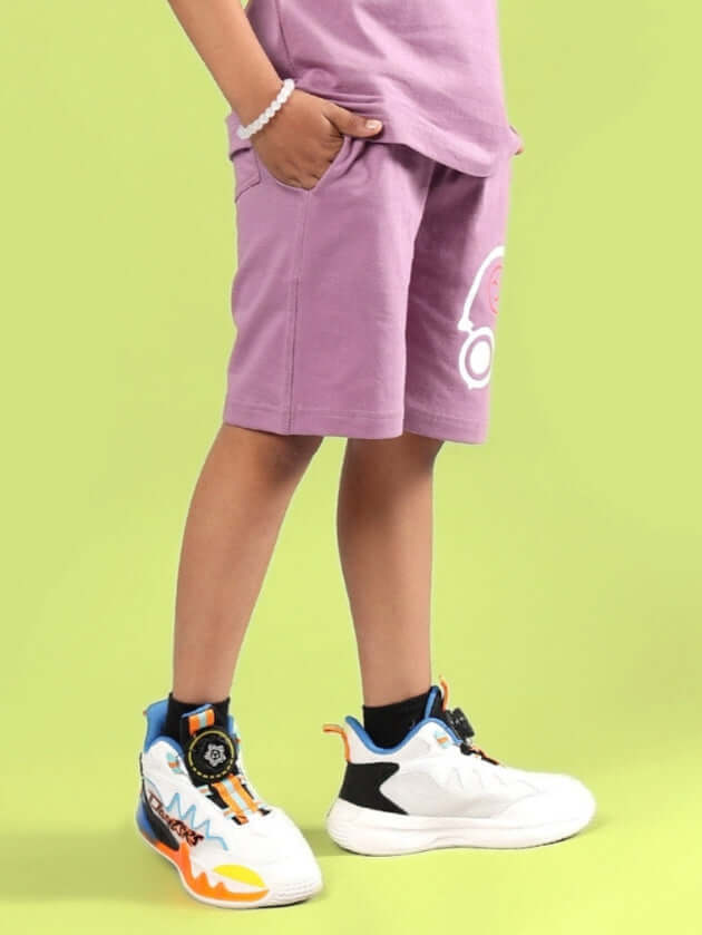 Child wearing STOIC SHORTS FOR BOYS & GIRLS PULM PURPLE against green background.