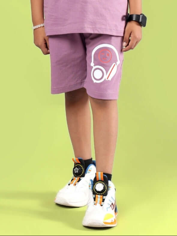 Child wearing STOIC SHORTS FOR BOYS & GIRLS PULM PURPLE against green background
