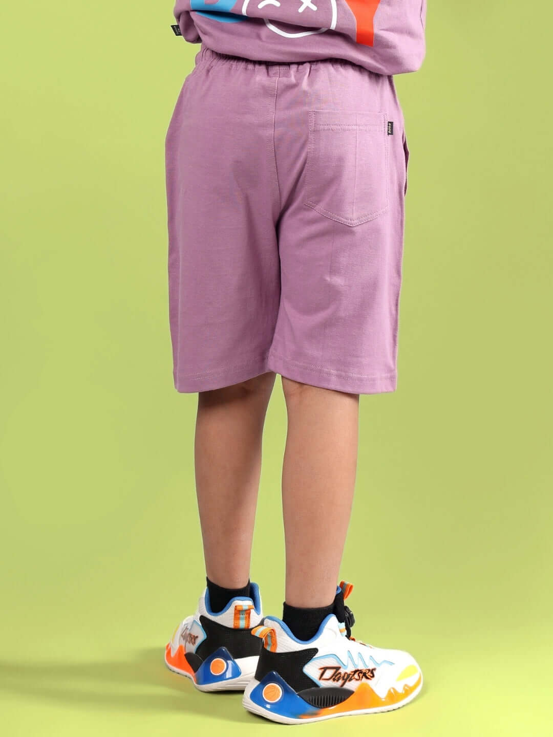 Child wearing STOIC SHORTS FOR BOYS & GIRLS PULM PURPLE, showcasing the back design against a green background.