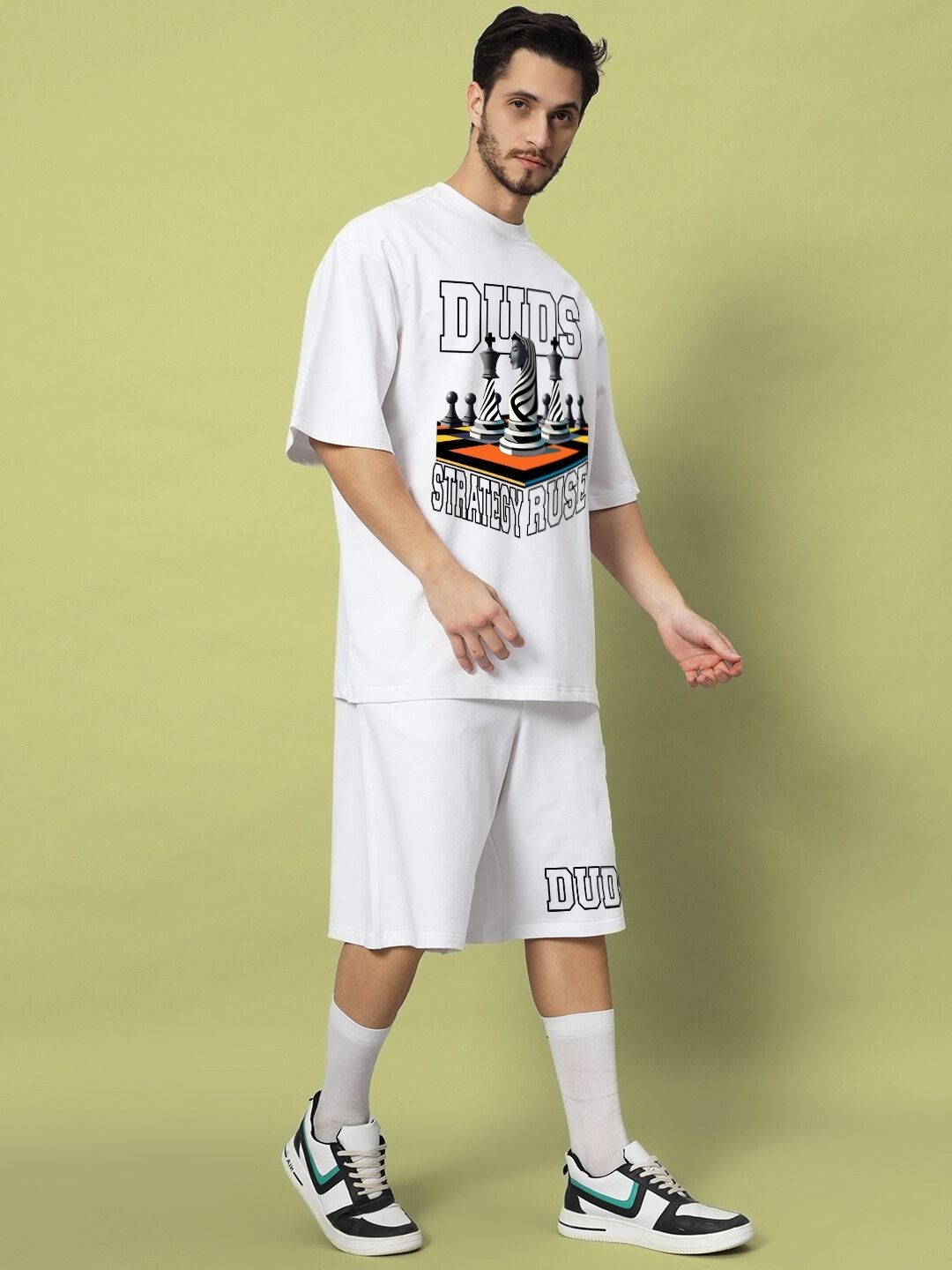 Model wearing STRATEGY RUSE CO-ORD SET WHITE with chess-themed design, walking confidently against a green background.