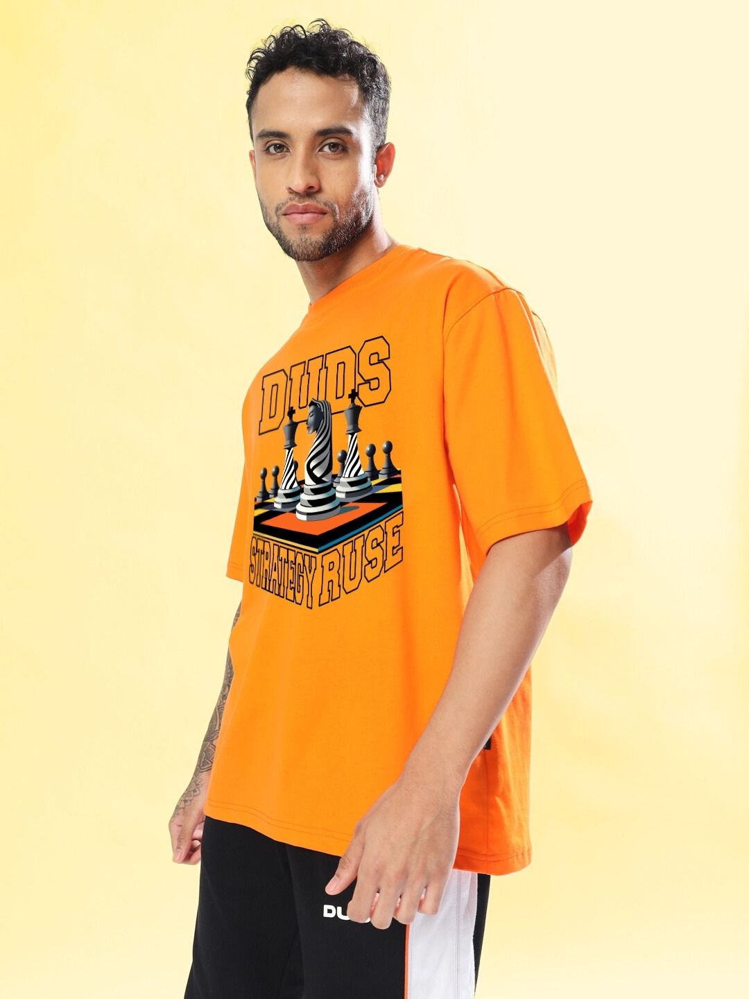 Model wearing STRATEGY RUSE OVER-SIZED T-SHIRT ORANGE against a yellow background