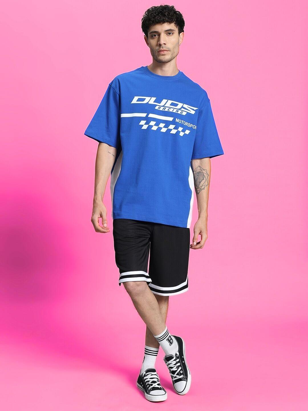 Model wearing Streak Regular Fit Black Shorts paired with a blue t-shirt, showcasing casual style on a pink backdrop.