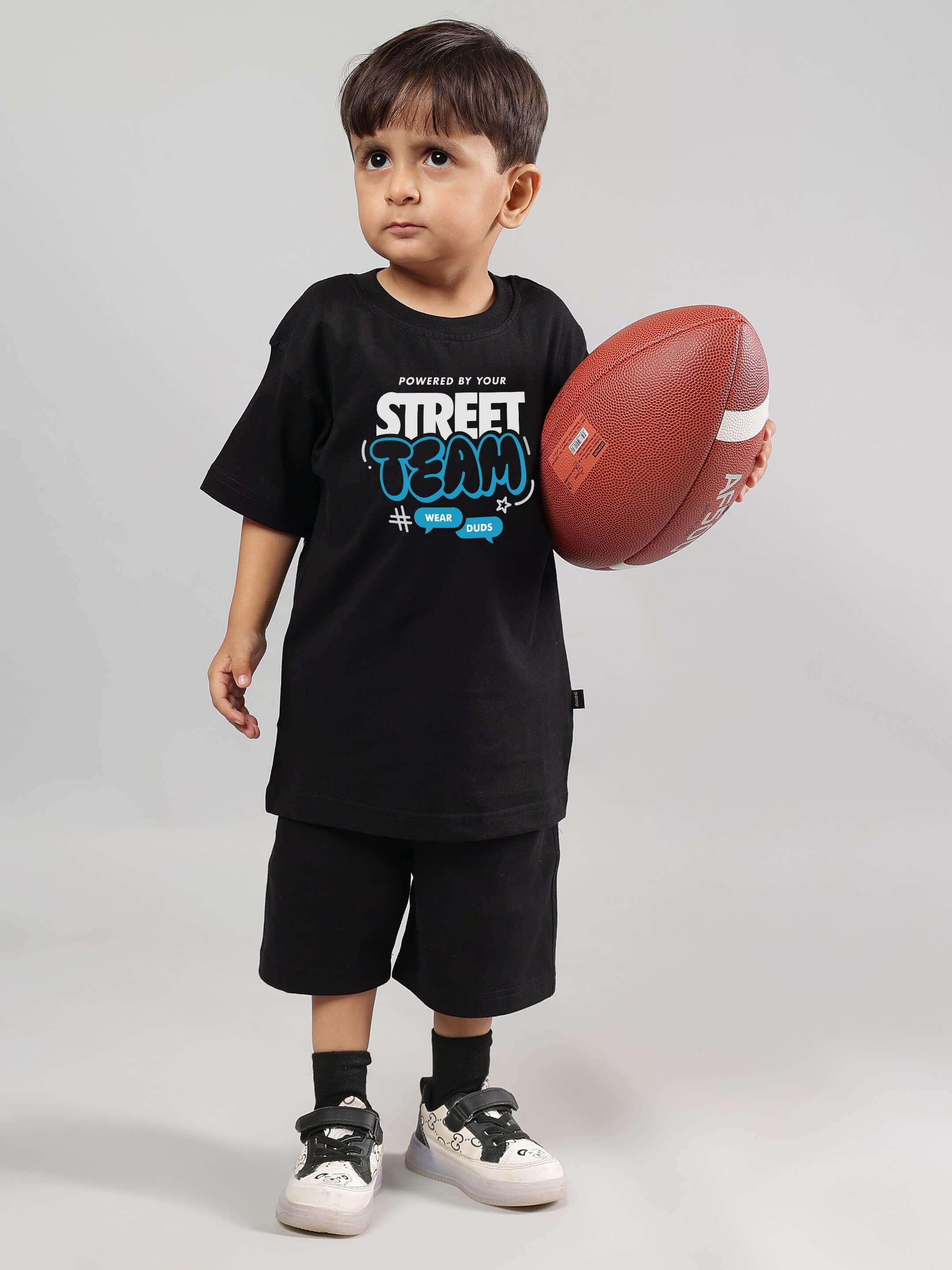 Child wearing black "Street Team" coord outfit holding a football, designed for boys and girls. Made to order by tailors at DUDS.