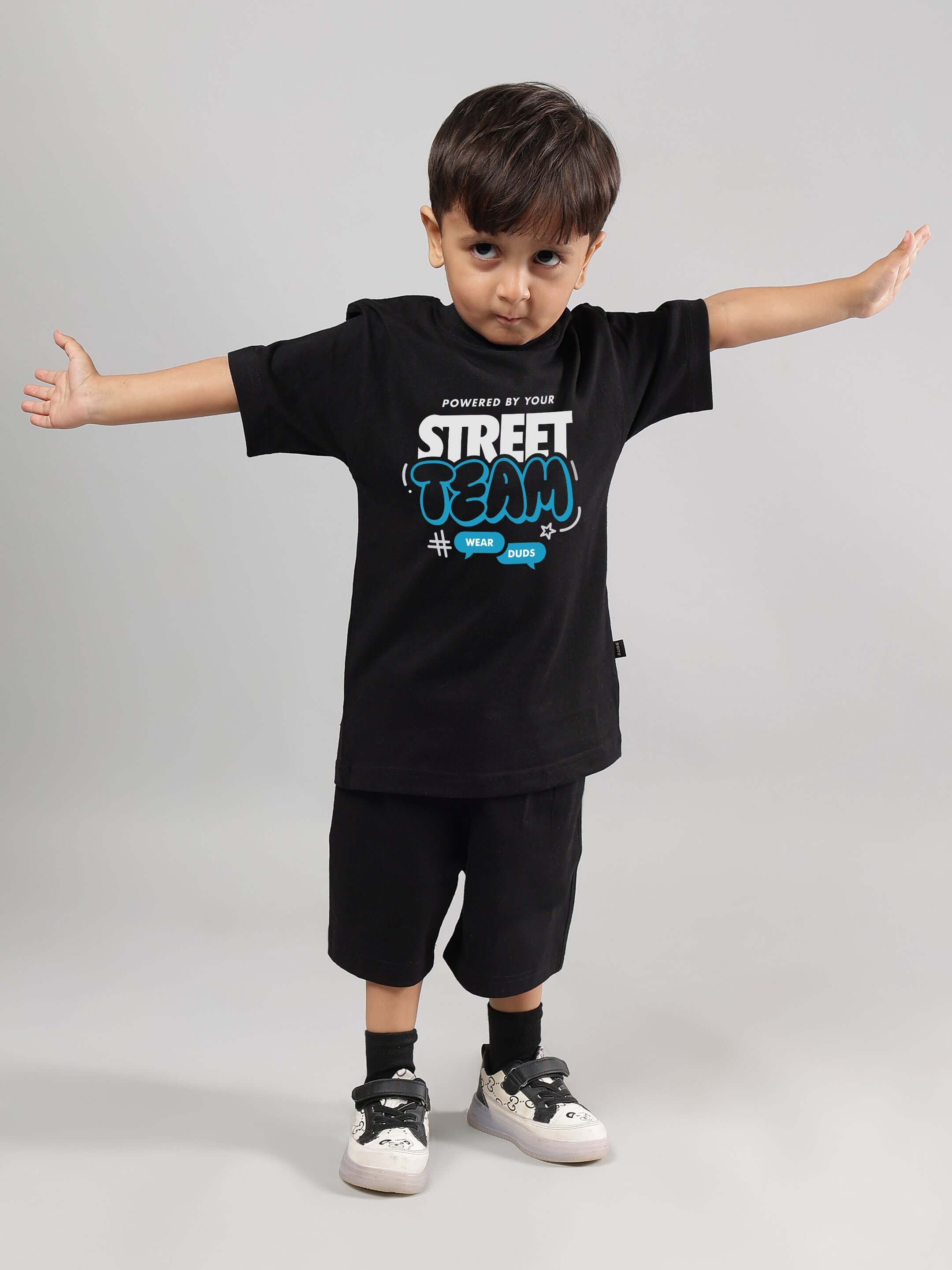 Child wearing black STREET TEAM T-shirt and shorts set by DUDS, arms open wide, white shoes. Made to order, customizable fit available.