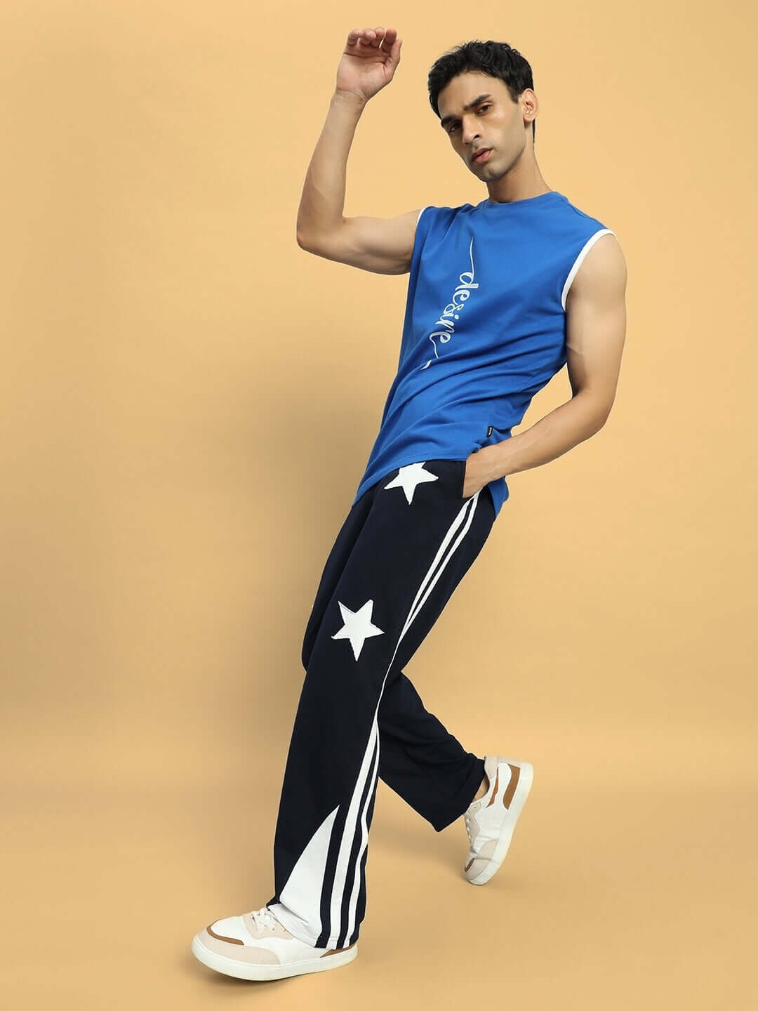 Person wearing navy blue relaxed joggers with white stars, styled with a blue sleeveless top, posing against a beige background.