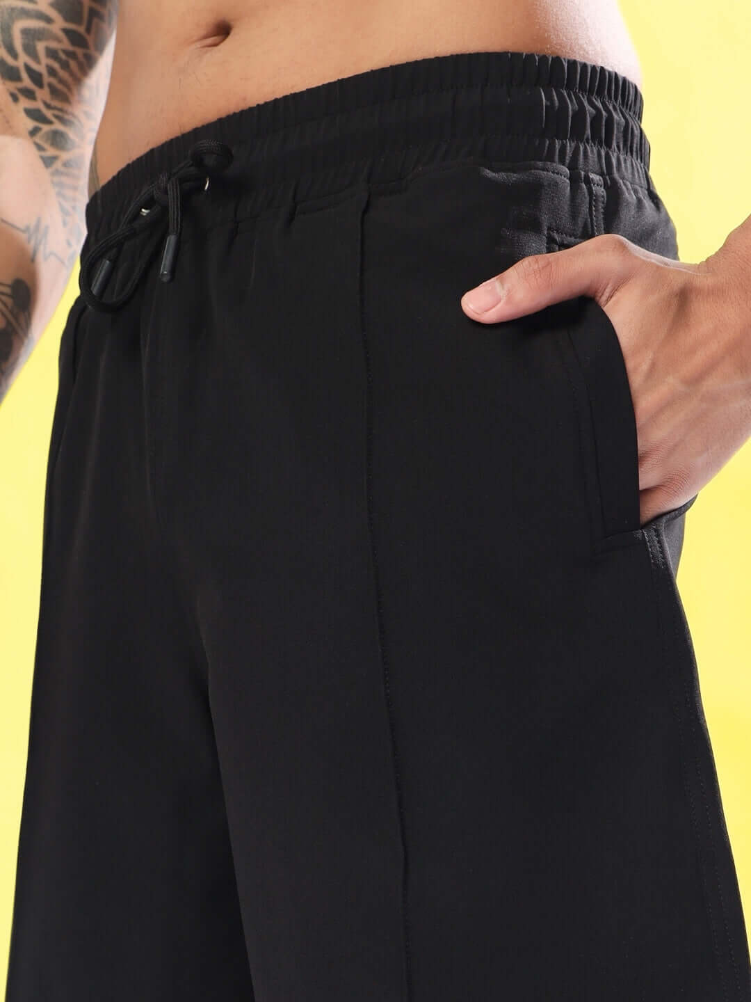 Close-up of black sturdy front plated shorts with drawstring waist, featuring a hand in the pocket, showcasing comfort and style.