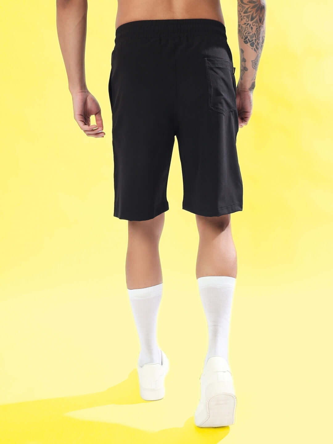 Back view of model wearing black sturdy front plated shorts with white socks, showcasing casual fit on a vibrant yellow background.