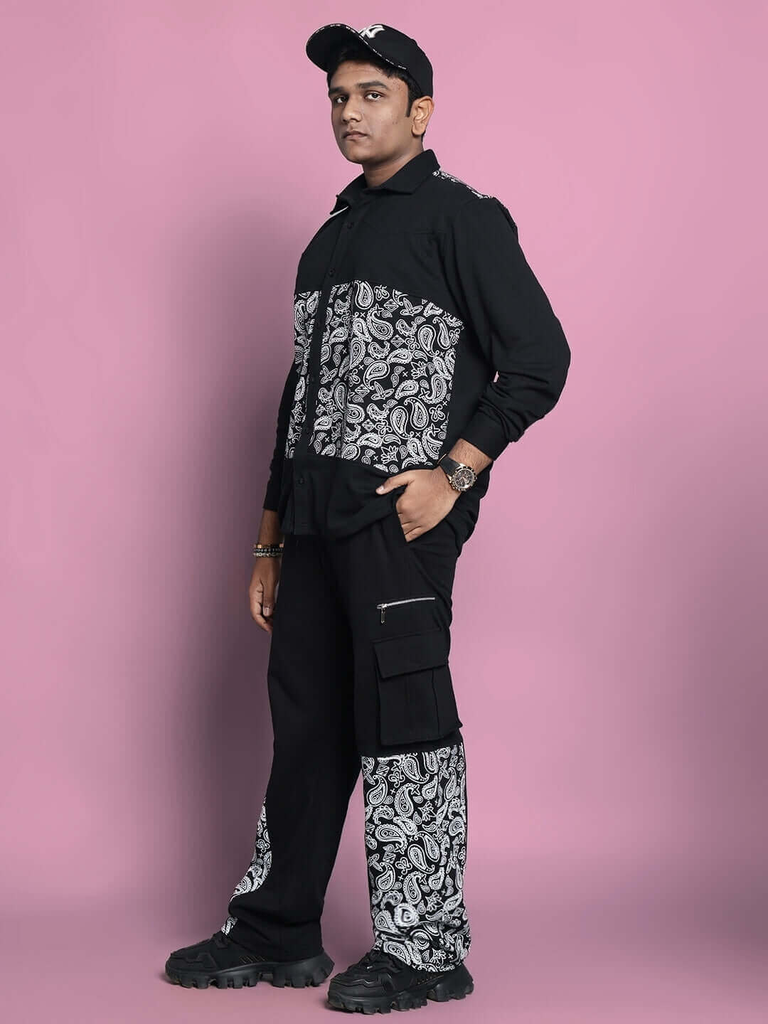 Man wearing black COVE co-ord set with paisley design, made from 100% cotton terry fabric, standing against a pink background.