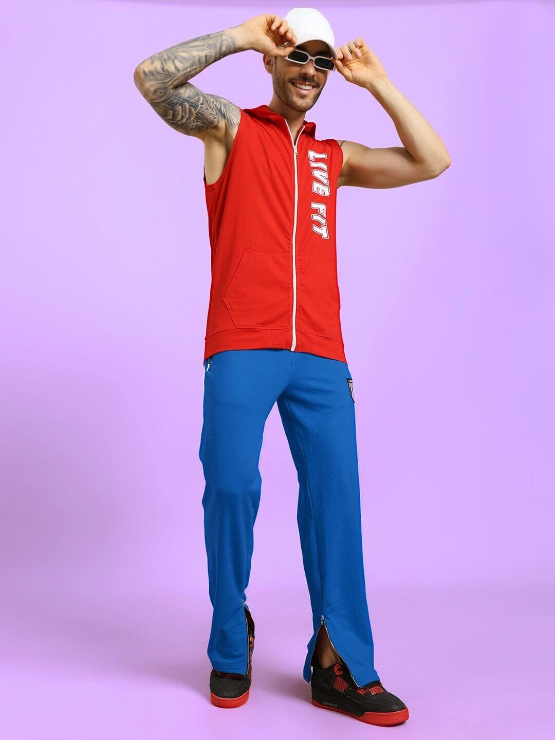 Man wearing ELEGANT RELAXED-FIT JOGGERS BLUE with red sleeveless jacket and black shoes, striking a casual pose on a purple background.