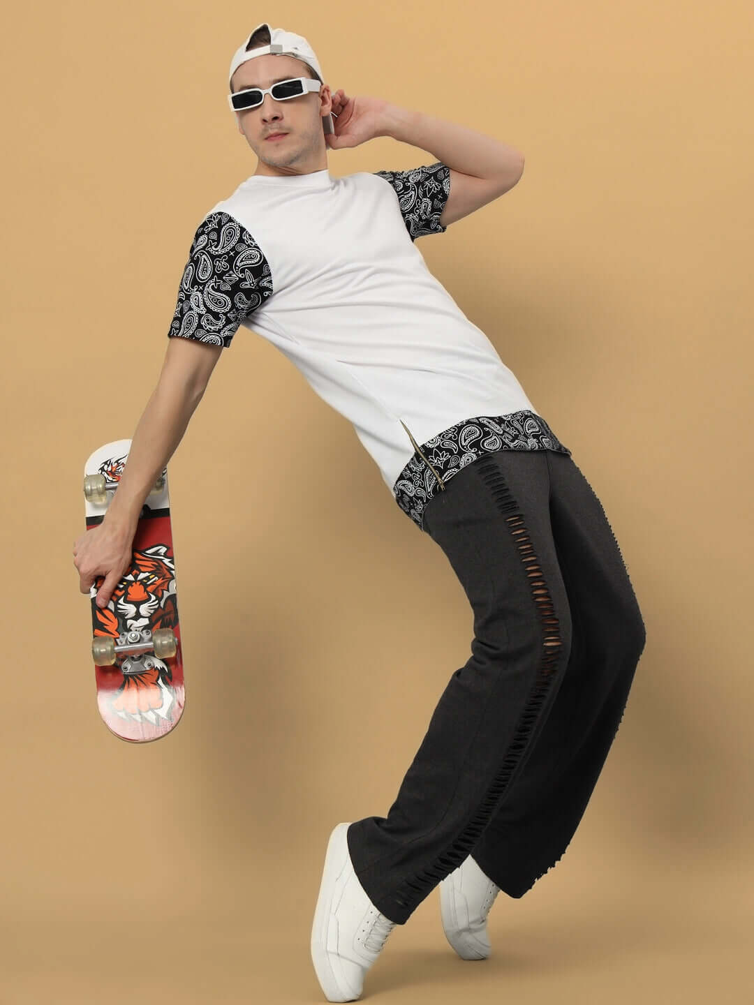 Person wearing stylish joggers and patterned shirt, holding a colorful skateboard against a neutral background.