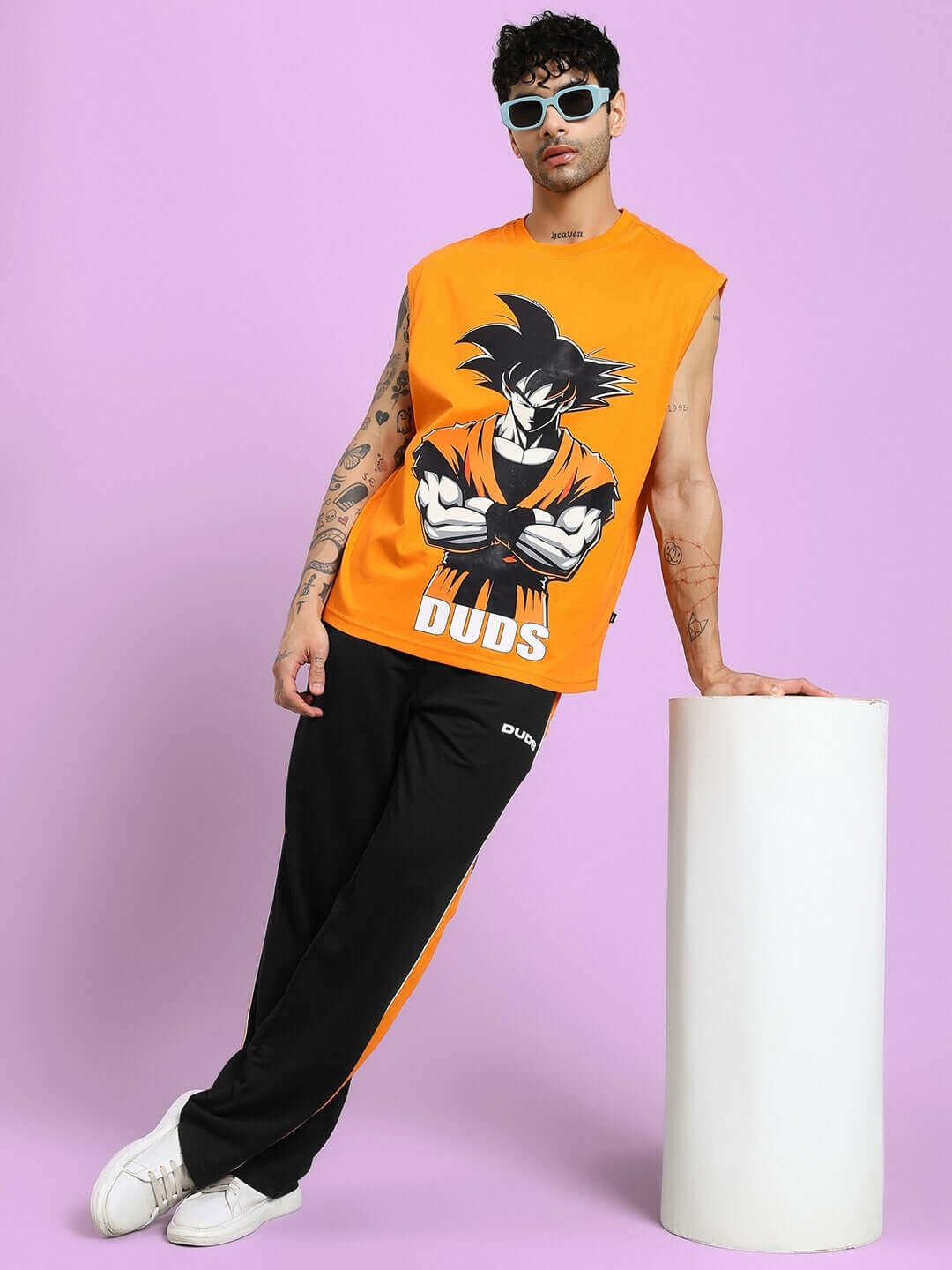 Man wearing SANFORD STRIPE JOGGERS IN BLACK with orange sleeveless top and sunglasses, leaning against a white pillar.