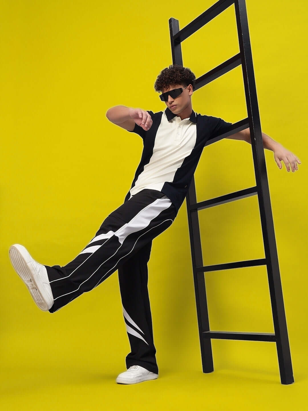 Model wearing Versatile Parachute Cargo Pants in black, posing against a yellow backdrop with a ladder.