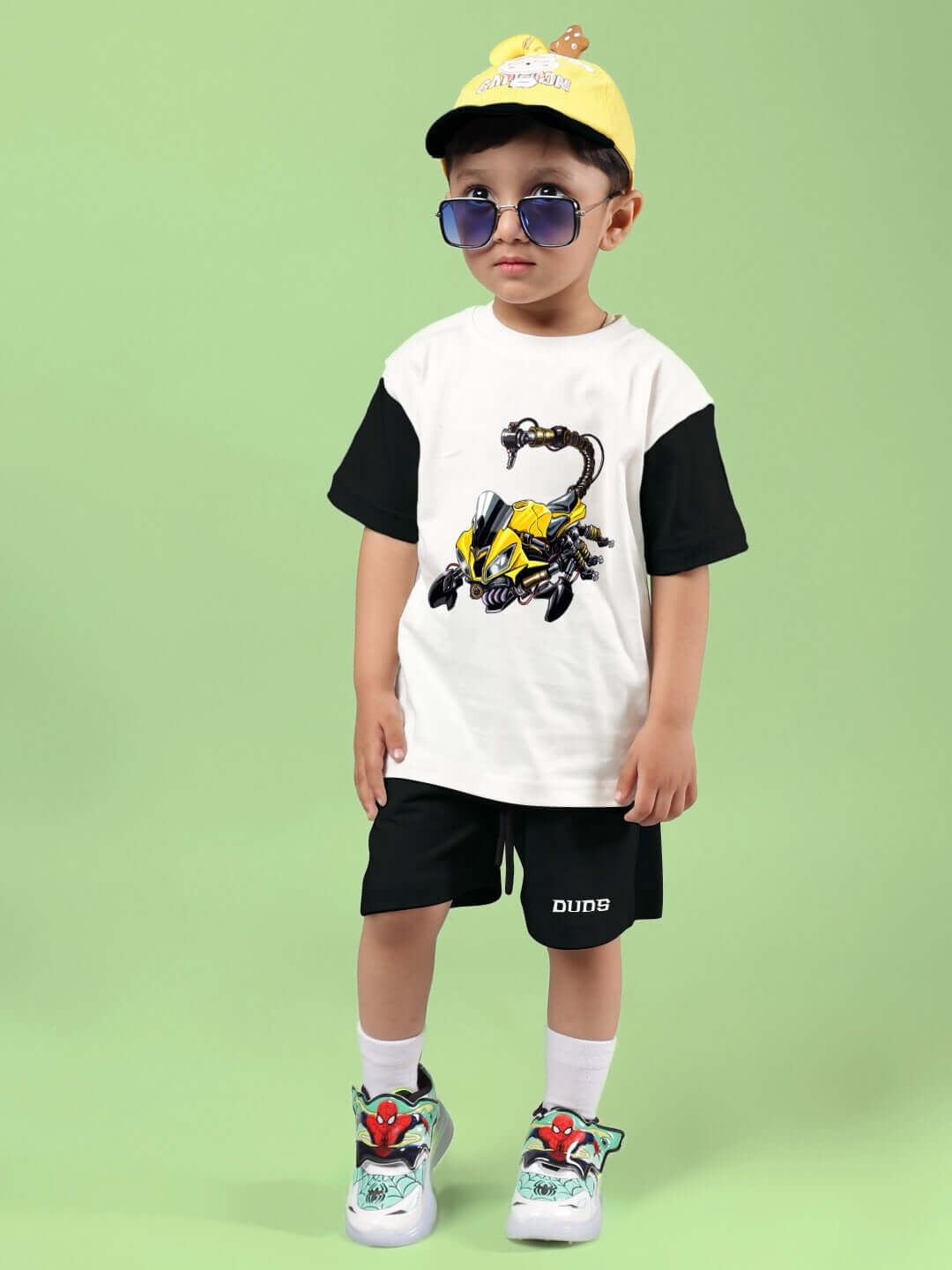 Child wearing STYLISH ROBOT CO-ORD FOR BOYS & GIRLS OFF WHITE BLACK with robot print t-shirt and shorts, green background