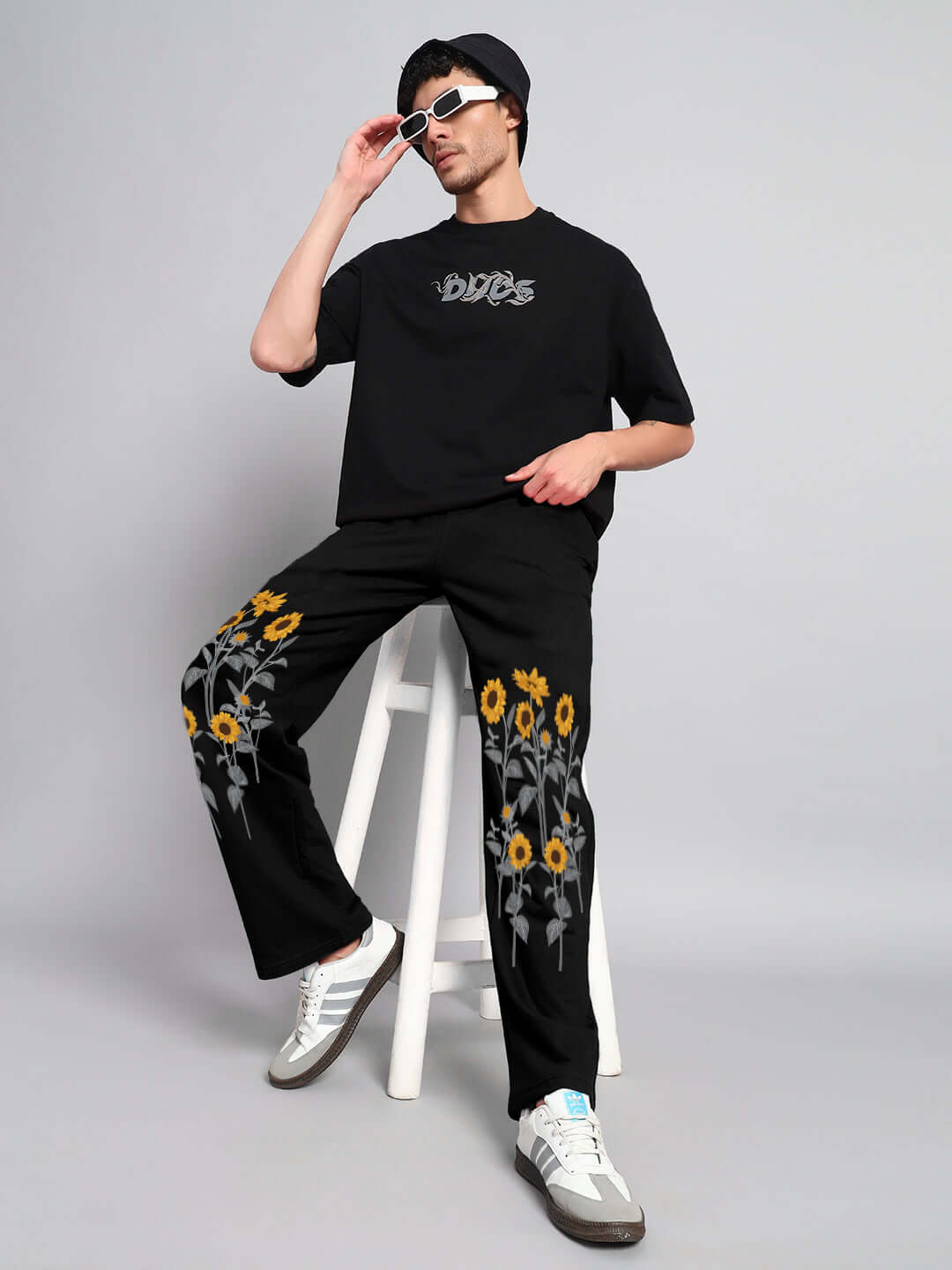 Man wearing SUNFLOWER RELAXED-FIT JOGGER BLACK with sunflower detailing, styled with a graphic shirt and sunglasses.