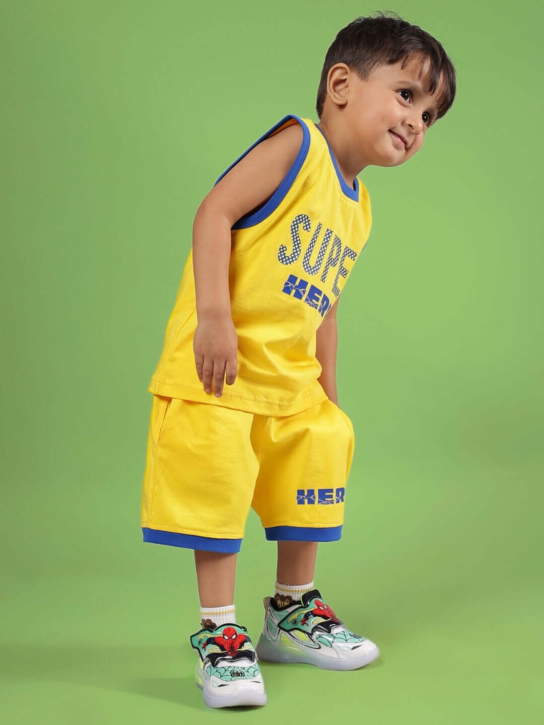 Young boy wearing SUPER HERO CO-ORD FOR BOYS & GIRLS YELLOW outfit with superhero design on green background.