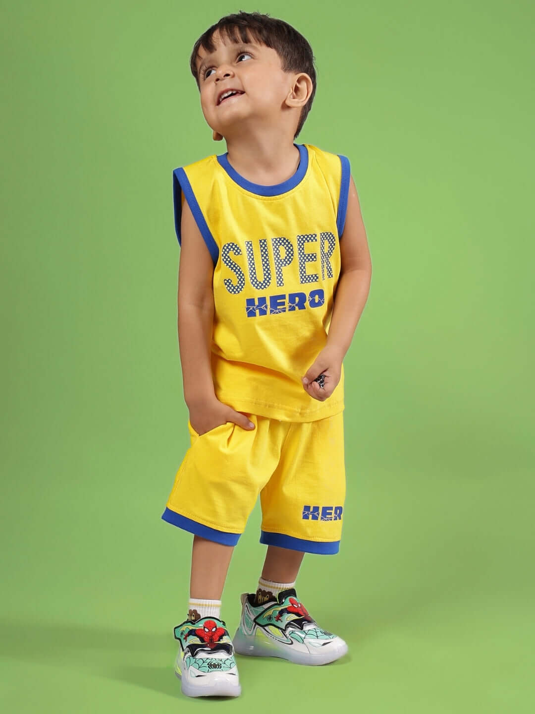 Child wearing SUPER HERO CO-ORD FOR BOYS & GIRLS YELLOW, standing with hands in pockets against a green background.