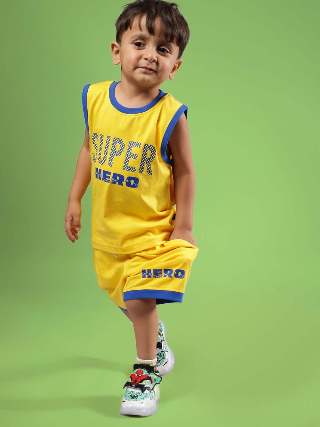 Kid wearing SUPER HERO SHORTS FOR BOYS & GIRLS YELLOW set with blue trim on green background