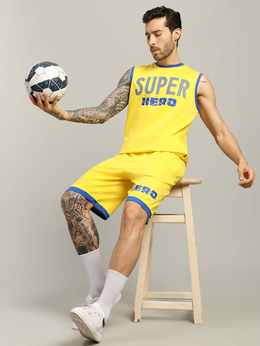 Man wearing SUPER HERO SUMMER SHORTS YELLOW sitting with a soccer ball, promoting customizable fit and handmade design.