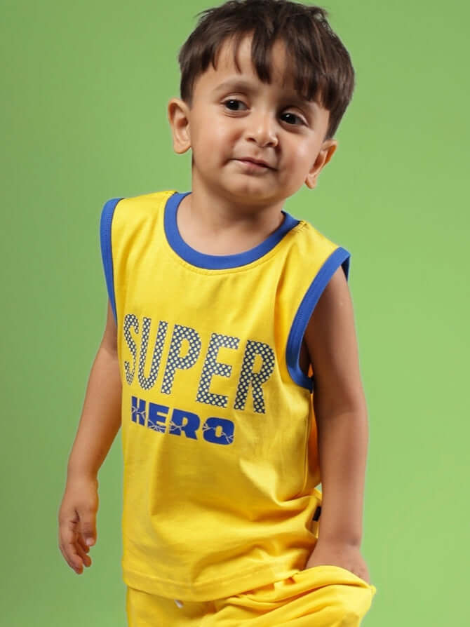 Young boy wearing SUPER HERO T-SHIRT FOR BOYS & GIRLS YELLOW with superhero design, standing against a vibrant green background.