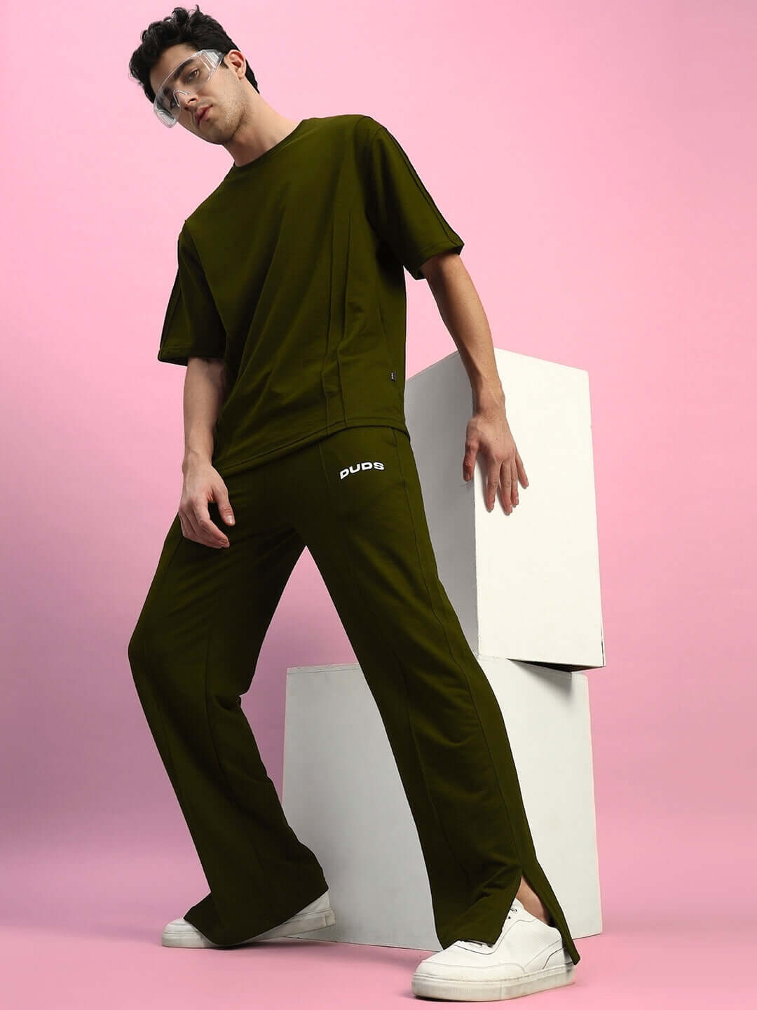 Model wearing olive green oversized t-shirt made from premium heavy gauge fabric, styled with matching pants, against pink background.